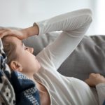 Upset depressed young woman lying on couch feeling strong headache